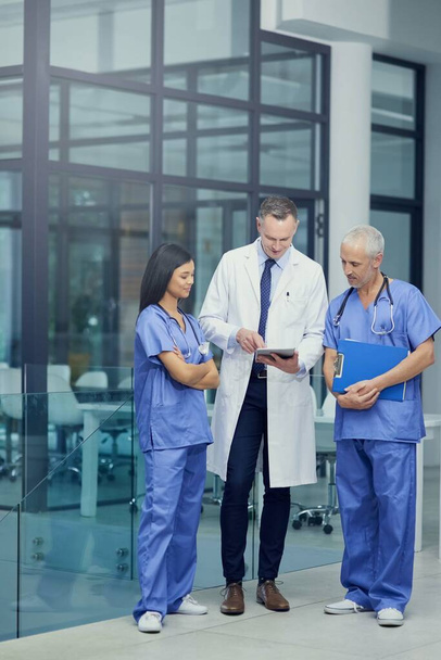 Porovnávám diagnózu. Snímek skupiny lékařů, jak spolu mluví přes digitální tablet, když stojí v nemocnici - Fotografie, Obrázek