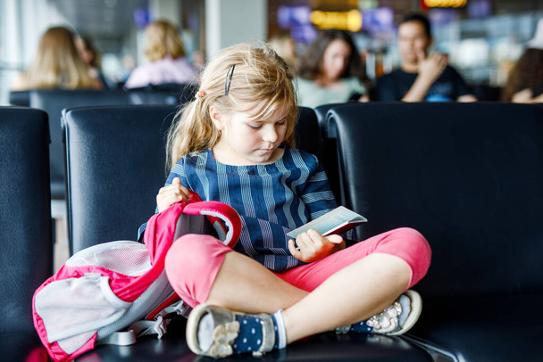 Küçük kız havaalanında büyük pencerede biniş için bekliyor. Pasaportu olan sevimli bir çocuk yaz tatiline gitmeyi dört gözle bekliyor.. - Fotoğraf, Görsel