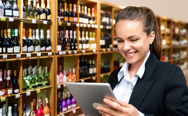 Young businesswoman checks commercial performance of her own liquor store using digital tablet.	 - Foto, imagen