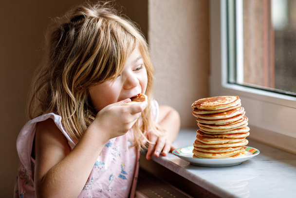 Little happy preschool girl with a large stack of pancakes for breakfast. Positive child eating healthy homemade food in the morning - Photo, Image