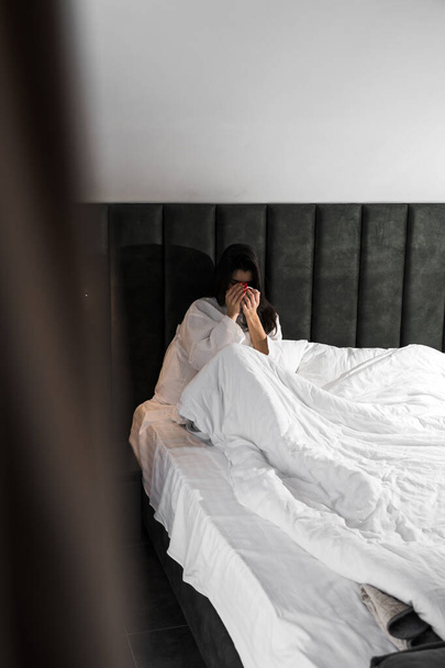 Uma mulher agradável acorda em um quarto de hotel e desfruta da vista da janela no inverno. Café na cama. Conceito de férias de hotel - Foto, Imagem