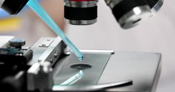Científico gotea muestra de líquido azul claro en una diapositiva del microscopio en primer plano de laboratorio. Estudio de líquidos tóxicos venenosos - Imágenes, Vídeo