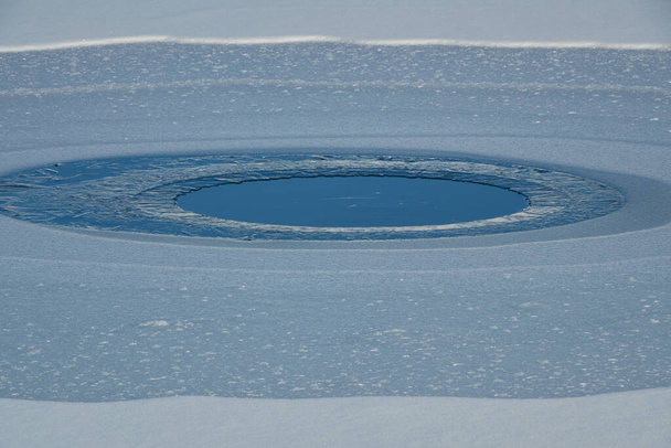 Παγωμένη κυκλική ορεινή λίμνη που περιβάλλεται από χιόνι - Φωτογραφία, εικόνα