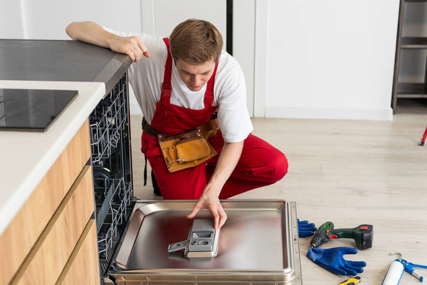 Concept συντήρηση των οικιακών συσκευών. Ο εργαζόμενος καθαρίζει το φίλτρο στο πλυντήριο πιάτων. Τεχνικός επισκευής αρσενικών φίλτρων υπολειμμάτων τροφίμων. - Φωτογραφία, εικόνα