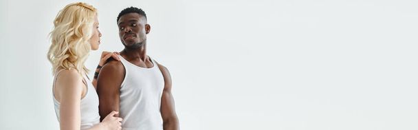 A young man and woman stand side by side in a studio, both wearing white tank tops on a grey background. - Photo, Image