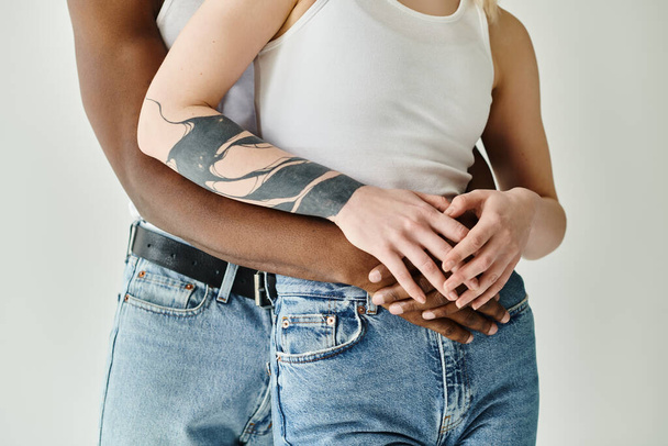 Un uomo con un tatuaggio sul braccio che tiene la mano di una donna, mostrando unità, amore e connessione tra una coppia multiculturale in uno studio su uno sfondo grigio. - Foto, immagini