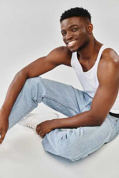 Ein junger afroamerikanischer Mann sitzt mit überkreuzten Beinen auf dem Boden in einer kühlen Position. - Foto, Bild