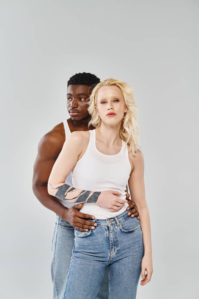 Ένα νεαρό διαφυλετικό ζευγάρι στέκεται δίπλα-δίπλα σε ένα στούντιο, αποπνέοντας ενότητα και σύνδεση σε ένα γκρίζο φόντο.. - Φωτογραφία, εικόνα