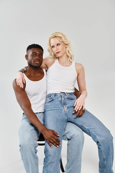 Ένα νεαρό διαφυλετικό ζευγάρι κάθεται με χάρη σε μια καρέκλα σε ένα στούντιο, επιδεικνύοντας ενότητα και αγάπη. - Φωτογραφία, εικόνα