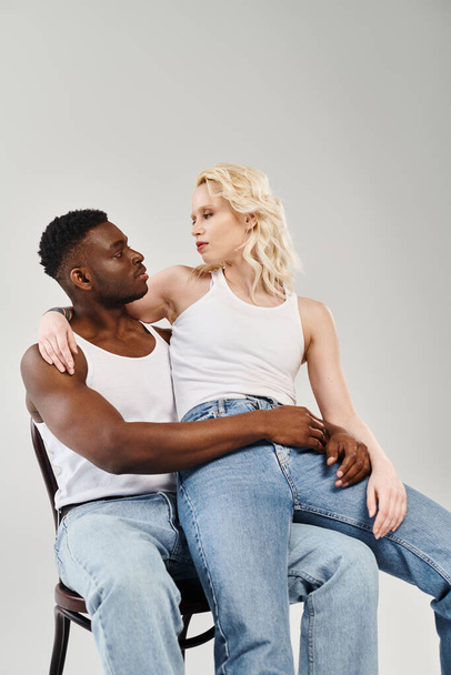 A young interracial couple leisurely seated on a chair in a studio against a grey background. - Photo, Image