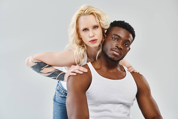 Um jovem e uma mulher de raças diferentes fazem uma pose juntos em um estúdio contra um pano de fundo cinza. - Foto, Imagem