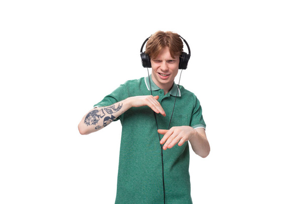 aranyos fiatal vörös hajú srác zöld pólóban zenét hallgat vezeték nélküli fejhallgatóval. - Fotó, kép