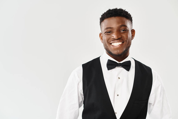 Handsome African American groom smiles joyfully at the camera, exuding charm in a stylish tuxedo against a grey studio backdrop. - Photo, Image