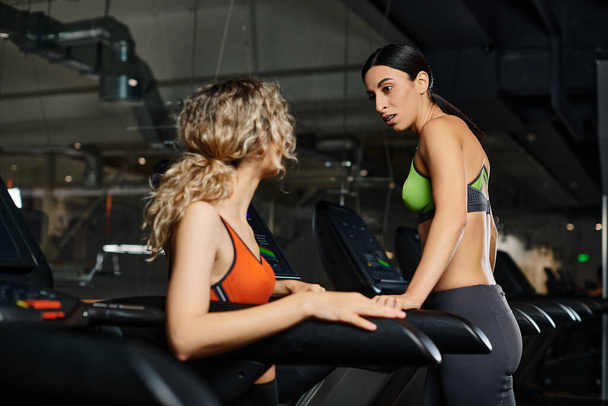 good looking energetic female coach and blonde client in sportwear exercising on treadmill in gym - Photo, Image