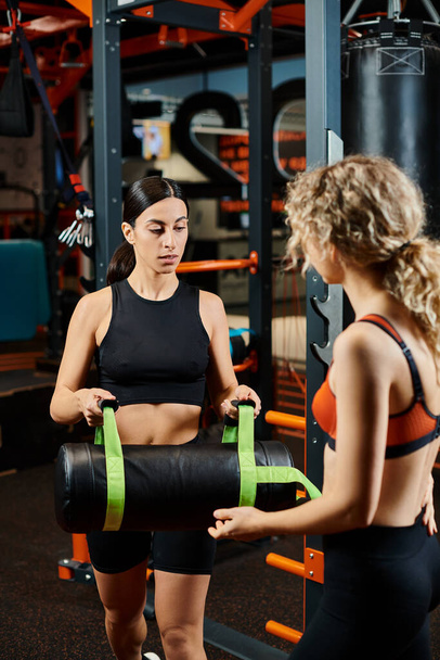 attractive sporty woman and her athletic female coach practicing with power bag while in gym - Foto, Imagem