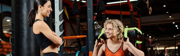 happy beautiful woman and her athletic female coach practicing with power bag while in gym, banner - Photo, Image