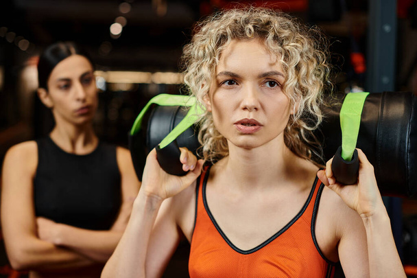 skupić się na blondynka atrakcyjne kobieta ćwiczenia z power bag z jej niewyraźne trener kobiet na tle - Zdjęcie, obraz