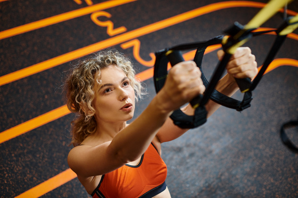 appealing blonde woman in comfortable sportwear exercising with pull ups equipment while in gym - Photo, Image