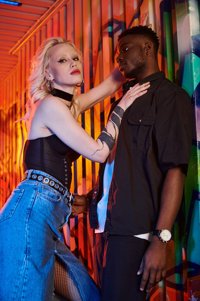 Una mujer rubia y un hombre afroamericano se unen en una calle urbana llena de coloridas paredes cubiertas de graffiti. - Foto, imagen