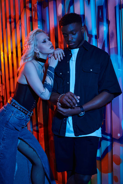 A blonde woman and an African American man stand side by side on an urban street with graffiti-covered walls. - Photo, Image