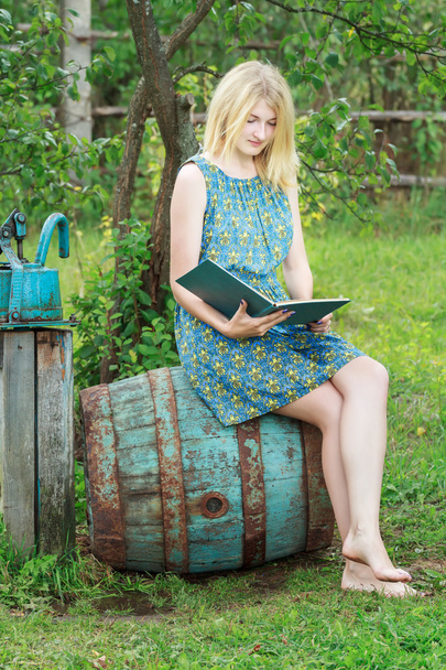 Студентська дівчина в саду читає книгу з блакитною обкладинкою
 - Фото, зображення