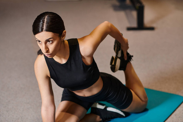 привлекательная атлетичная женщина в черной спортивной форме растягивает мышцы на тренажерном коврике во время тренировки - Фото, изображение
