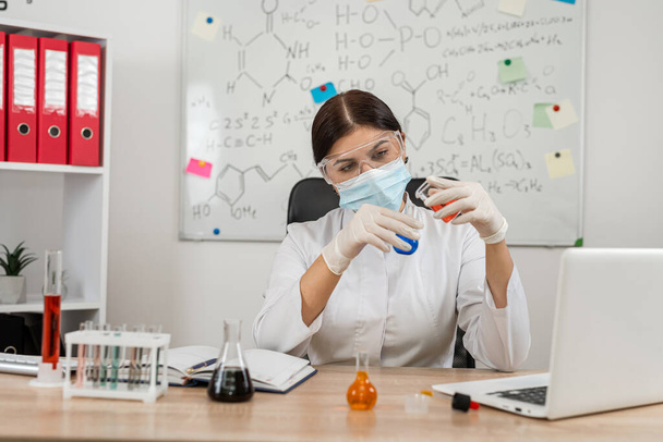 Blanke vrouwelijke wetenschapper gemengd vloeistof uit fles in bekerglas. Experiment biochemie en moleculaire biologie - Foto, afbeelding