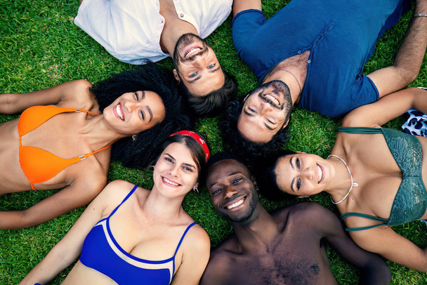 Rozmanitá skupina mladých přátel v plavkách ležících na trávě, sdílejících chvíle radosti a relaxace. - Fotografie, Obrázek