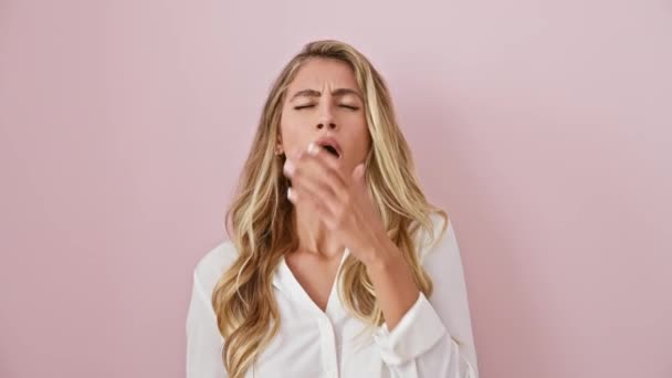 Beautiful blonde woman, overwhelmed by sleepiness, exhibiting a huge yawn. standing bored and tired over an isolated pink background, her hand does its best to cover her yawning mouth. - Footage, Video