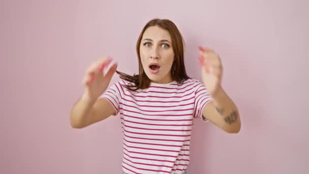 Startled young brunette girl in striped tshirt holds head in shock. crazy scared expression, mouth open wide in surprise over pink isolated background. - Footage, Video