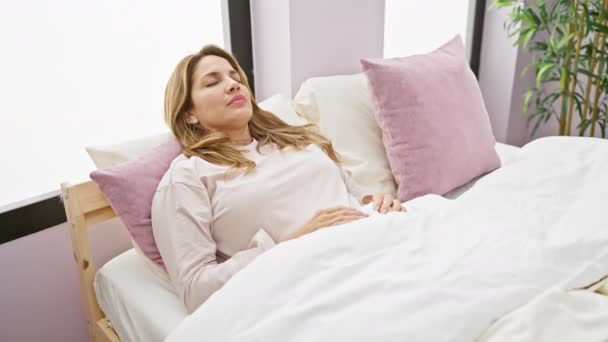 Szczęśliwa latynoska kobieta budzi się w swojej jasnej sypialni, emanując pięknem i pozytywnością w przytulnej porannej scenie. - Materiał filmowy, wideo