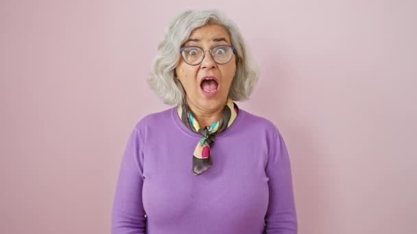Божевільна сіро-волохата жінка набиває щоки в своєрідному пуху, виділяючись на ізольованій рожевій стіні, в окулярах з невпевненістю! - Кадри, відео