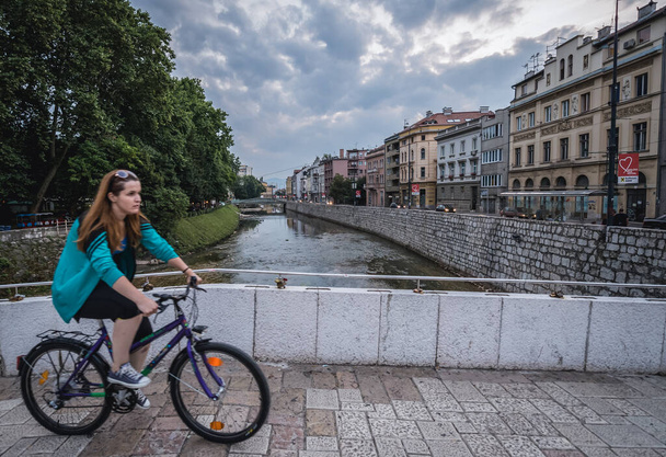 サラエボ,ボスニア,ヘルツェゴビナ - 2015年8月23日:サラエボ市のミラヤフラ川を渡るラテンブリッジで自転車に乗る少女 - 写真・画像
