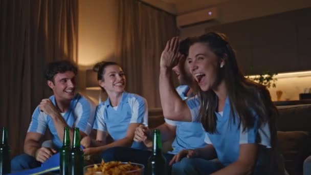 Podekscytowani przyjaciele radujący się bramką dając pięć w domu wieczorem zbliżenie. Szczęśliwi emocjonalni fani oglądają football w TV siedząc na kanapie. Śmiejący się ludzie świętujący zwycięstwo drużyny na mistrzostwach sportowych - Materiał filmowy, wideo