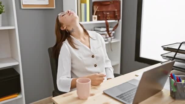 Junge Brünette, die gelangweilt und müde aussieht und mit verschränkten Armen über Depressionen nachdenkt, während sie im Büro Laptop benutzt - Filmmaterial, Video