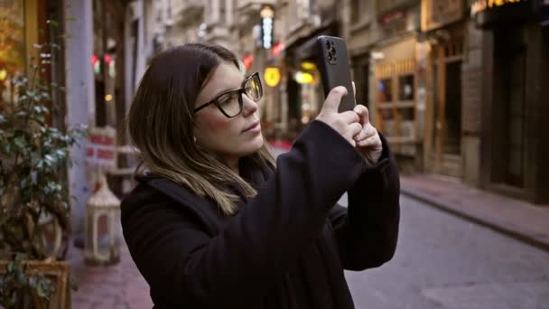 Een jonge vrouw neemt een selfie in een historische straat in Istanbul, omgeven door stadsleven en bezienswaardigheden. - Video