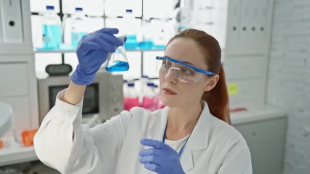Una científica enfocada examinando un líquido azul en un frasco en un laboratorio. - Metraje, vídeo