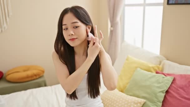 Une jeune femme asiatique appliquant des soins de la peau dans sa chambre brillamment éclairée, illustrant la beauté et le bien-être à la maison. - Séquence, vidéo