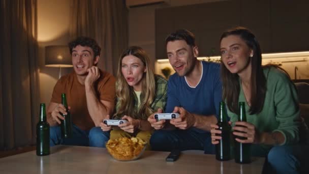 Ομάδα τυχερών παιχνιδιών απολαμβάνουν video play στο σπίτι το βράδυ. Ενθουσιασμένοι νέοι άνθρωποι που κατέχουν joysticks ανταγωνίζονται σε videogame κάθεται άνετο καναπέ μαζί. Συναισθηματικοί χαρούμενοι φίλοι που διασκεδάζουν στο στέκι του Σαββατοκύριακου. - Πλάνα, βίντεο