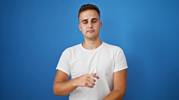 Portré egy magabiztos fiatal spanyol férfi áll szemben egy sima kék háttér visel egy fehér ing. - Felvétel, videó