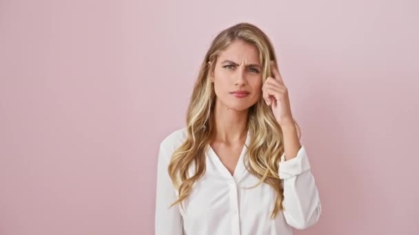 Verveelde jonge blonde vrouw draagt shirt wijst vinger naar het voorhoofd, geïsoleerd over roze, advertentie met open palm tonen kopieerruimte. expressieve en lastige houding. - Video