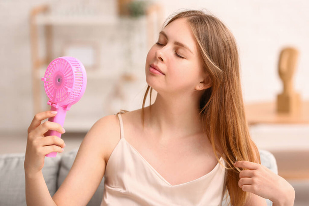 Beautiful young woman with handheld mini fan at home - Photo, Image