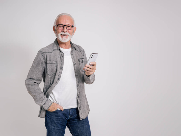 Sorrindo executivo masculino sênior mensagens de texto sobre o telefone celular e posando com confiança no fundo branco - Foto, Imagem