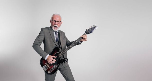 Emocionado músico de rock senior en traje cantando con la boca abierta y tocando la guitarra sobre fondo blanco - Foto, Imagen