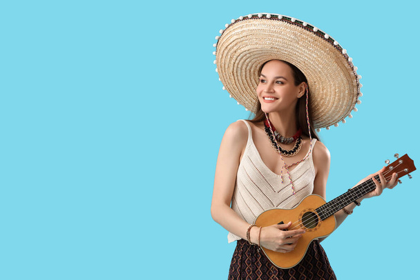 Mooie vrouw in sombrero hoed en met gitaar op lichtblauwe achtergrond - Foto, afbeelding