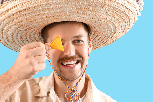 Счастливый молодой мексиканец в сомбреро и с начос на синем фоне - Фото, изображение