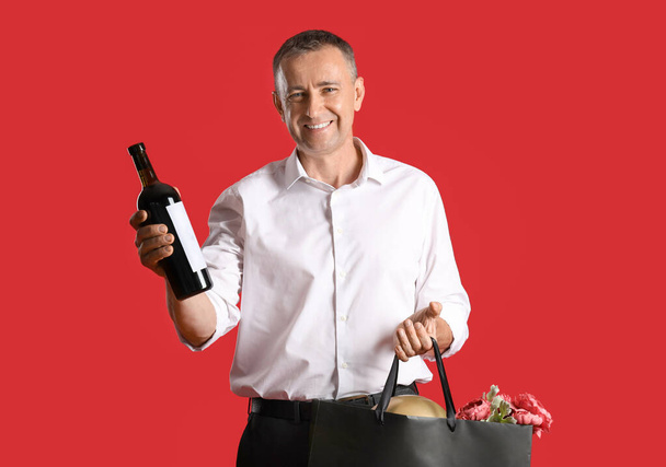 Älterer Mann mit Flasche Wein und Einkaufstasche auf rotem Hintergrund - Foto, Bild