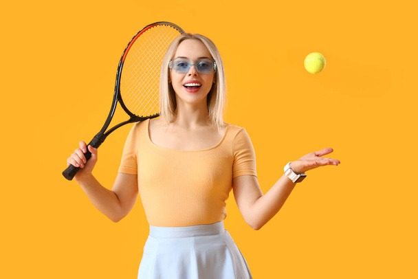 Sarı arka planda tenis raketi ve topu olan zarif genç bir kadın. - Fotoğraf, Görsel