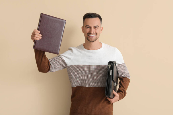 Joyeux jeune homme avec livre et mallette sur fond beige - Photo, image