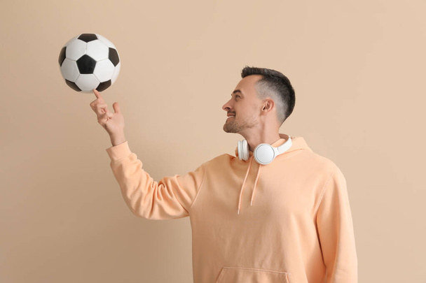 Šťastný mladý muž s fotbalovým míčem na béžovém pozadí - Fotografie, Obrázek